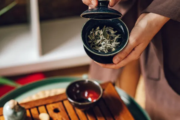 Hände halten einen Gaiwan mit Teeblättern und seinem Deckel