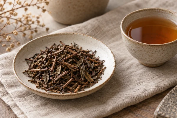 Braune geröstete Hojichablätter und Stängel neben kupferfarbenem Tee