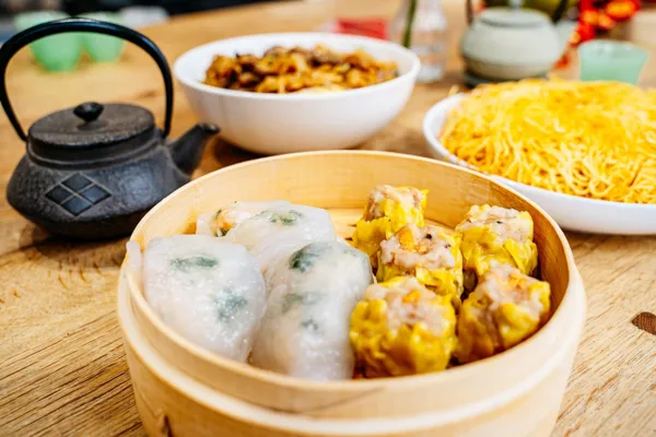 Dunkle Teekanne neben Dim Sum in einem Bambuskorb