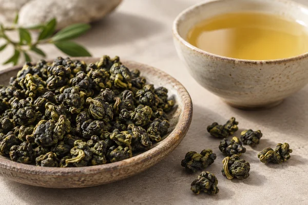 Pure gerollte Jin-Xuan-Blätter neben klarem goldenem Aufguss ohne Milch
