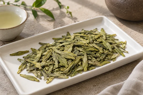 Flache gelbgrüne Longjing-Blätter auf einem weißen Tablett