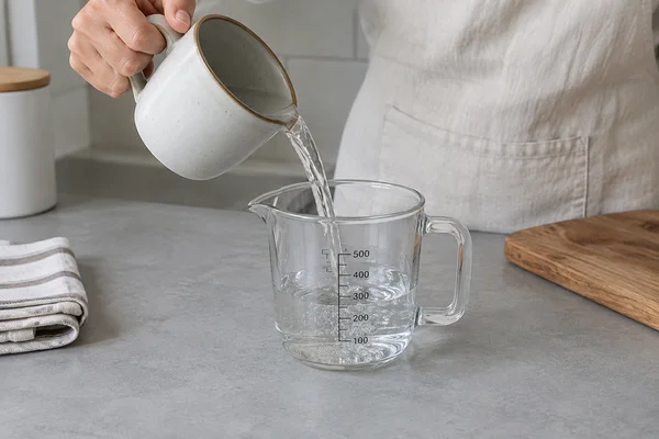 Wasser wird aus einer Tasse in einen Messbecher gegossen