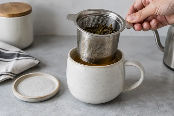 Ein großes Teesieb wird aus einer Keramiktasse gehoben