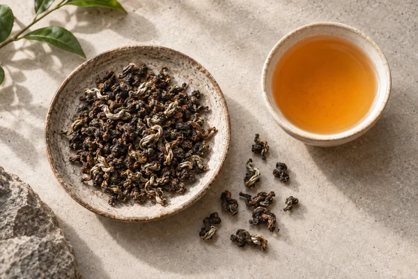 Braune, rötliche und silbrig gespitzte Oriental-Beauty-Blätter neben goldorangem Tee
