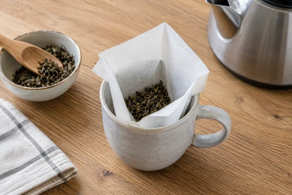Ein offener Papierfilter mit wenig losen Teeblättern in einer Tasse