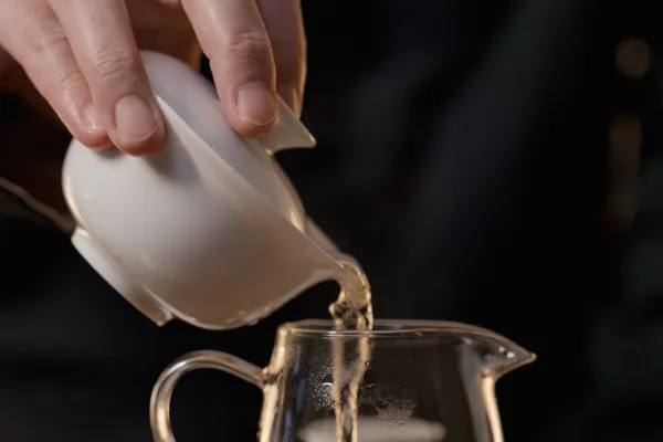 Tee wird aus einem Gaiwan in eine Servierkanne aus Glas gegossen