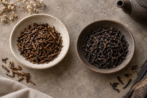 Gerösteter Hojicha und geräucherter Schwarztee getrennt mit ihren Tassen angeordnet