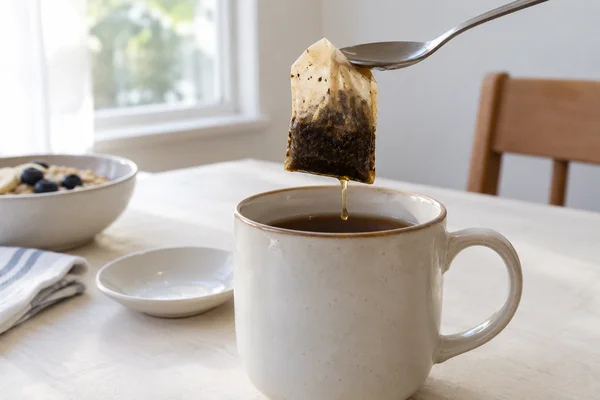 Ein nasser Teebeutel liegt auf einem Löffel über einer Tasse
