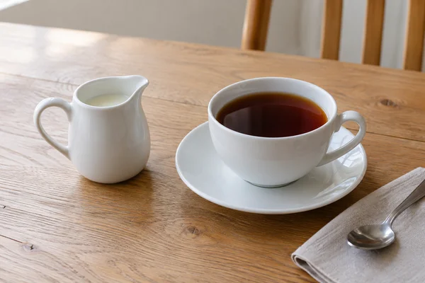 Ein Milchkännchen steht neben einer fertig aufgegossenen Tasse Schwarztee