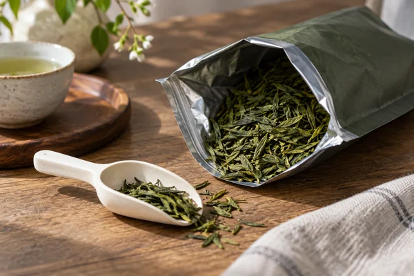 Offene Teepackung mit trockenen grünen Blättern und sauberem Löffel