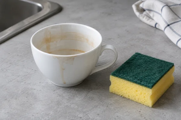 Eine Tasse mit sichtbarem Teerand neben einem Reinigungsschwamm