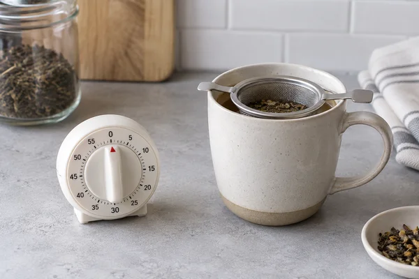 Ein Küchentimer neben einer Tasse mit Teesieb